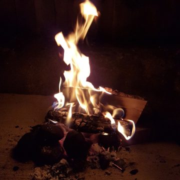 A small fire burns with bright flames atop dark logs and coals at night.
