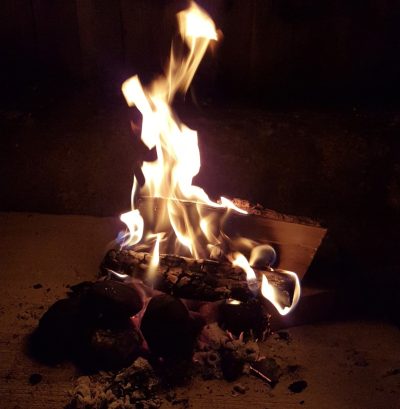 A small fire burns with bright flames atop dark logs and coals at night.